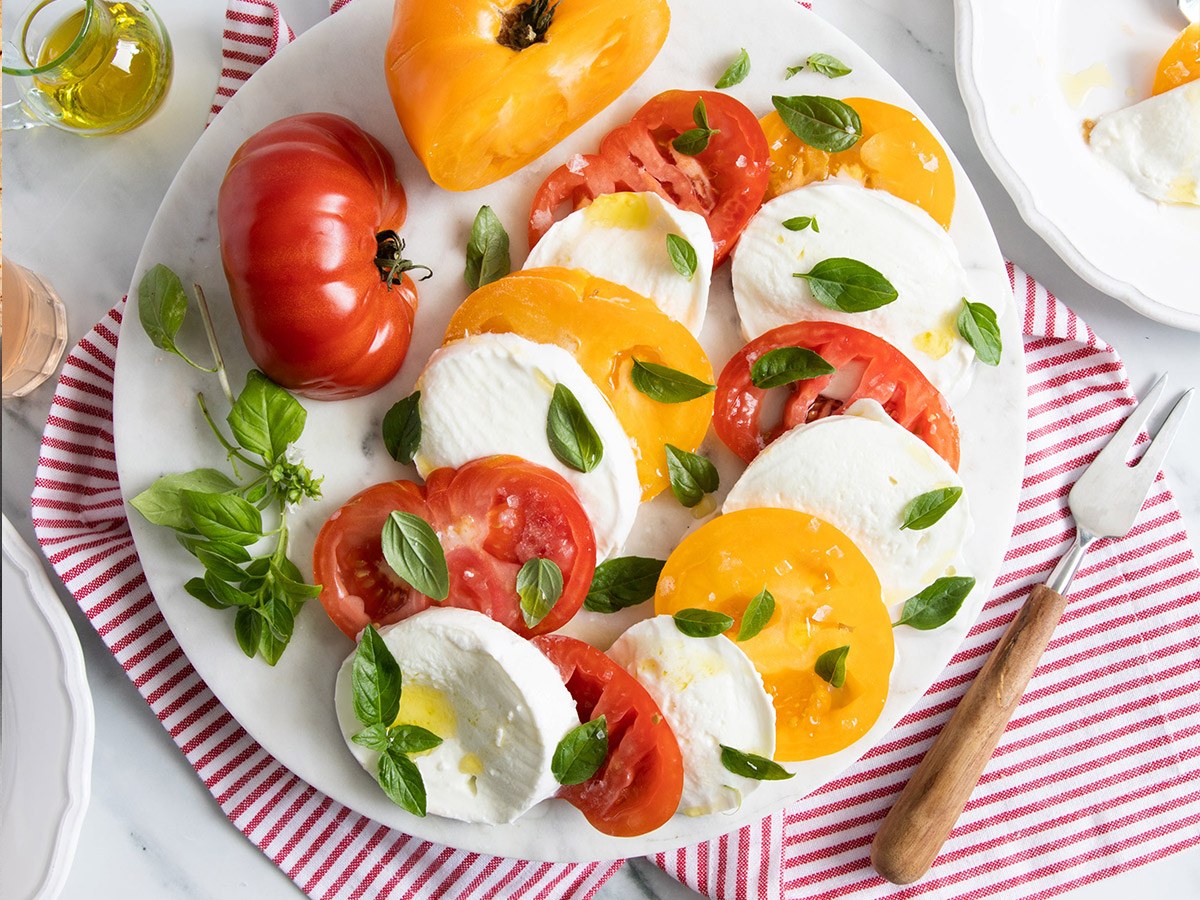 Sliced fresh mozzarella layered with red and yellow heirloom tomatoes and basil on a marble platter