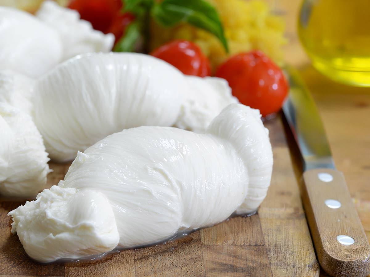 Hand-tied fresh mozzarella nodini on a wooden board with cherry tomatoes, basil and olive oil